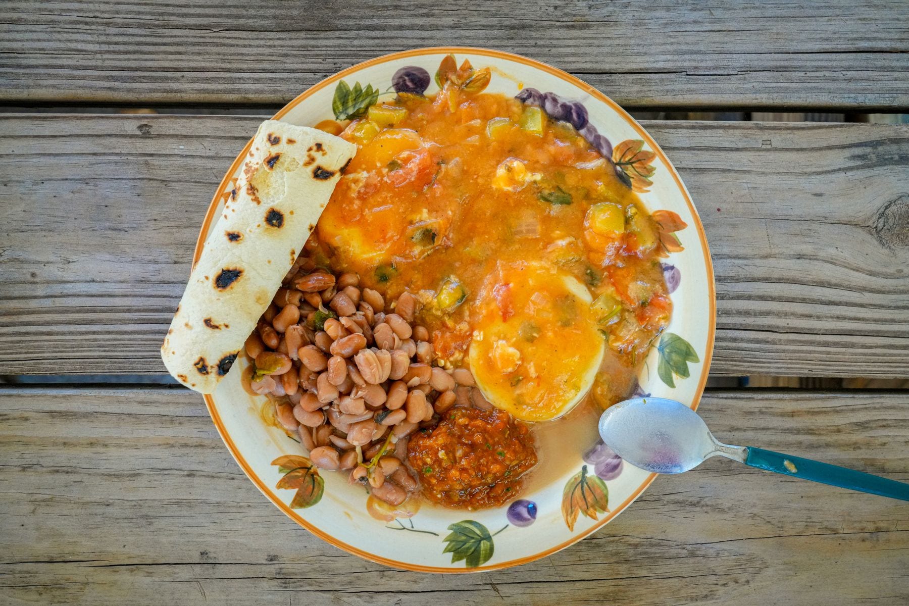 Plato de desayuno con huevos, frijoles, salsa y tortillas sobre una mesa de madera